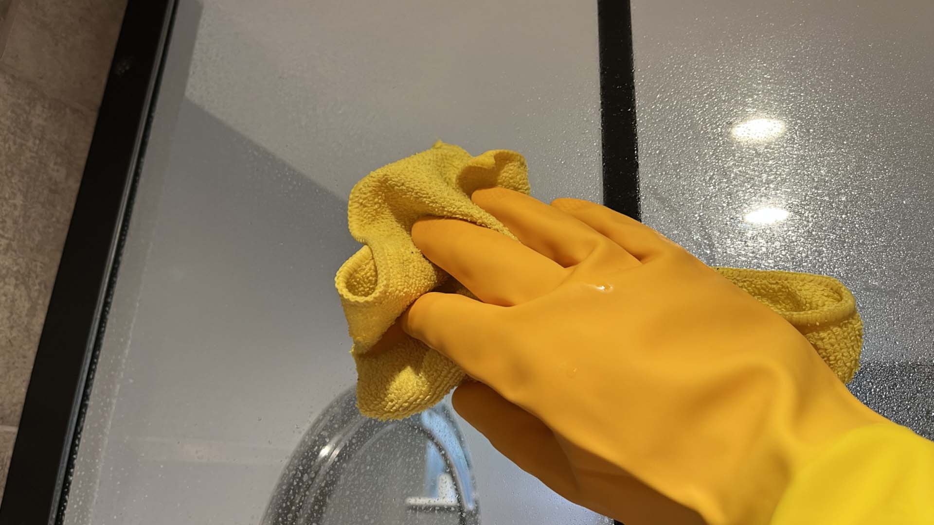 A hand wearing cleaning gloves wiping a mirror
