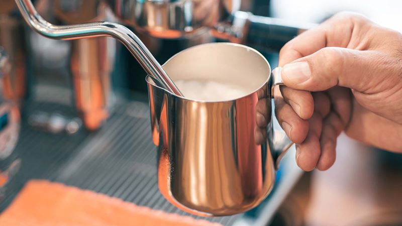 Barista is using high pressure steam operated milk frother to prepare a coffee milk.