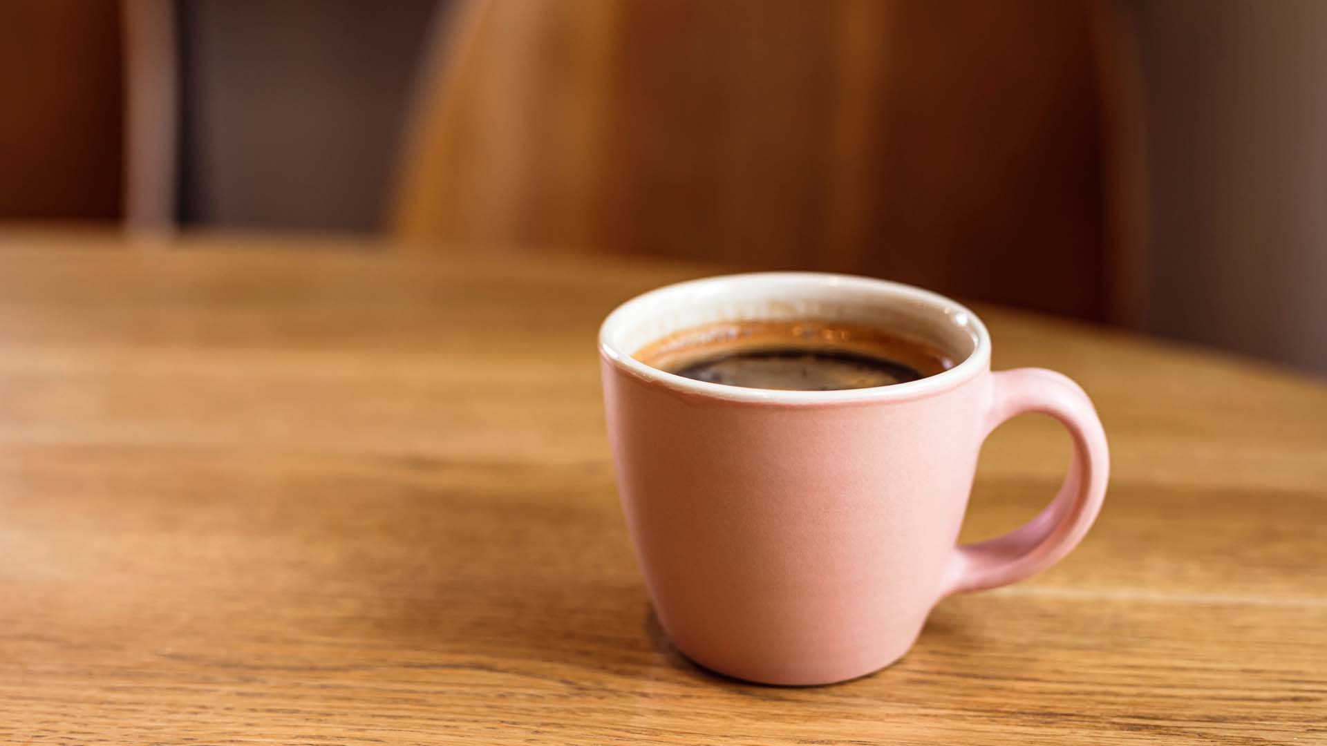 Cup of coffee in a pink mug on a wooden table