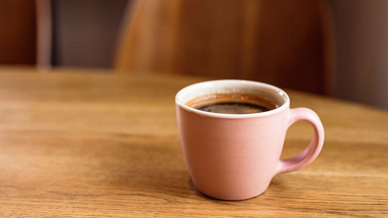 Cup of coffee in a pink mug on a wooden table