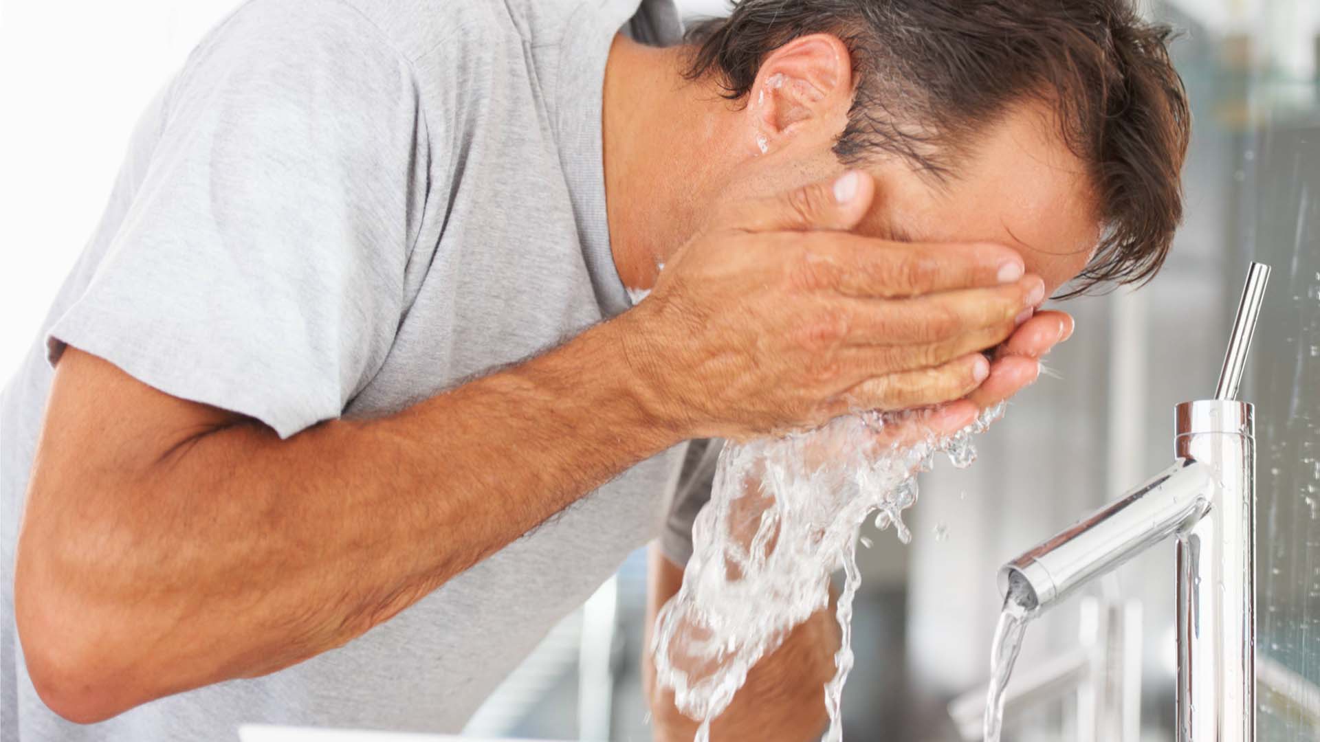 A man splashing his face with cold water over a basin