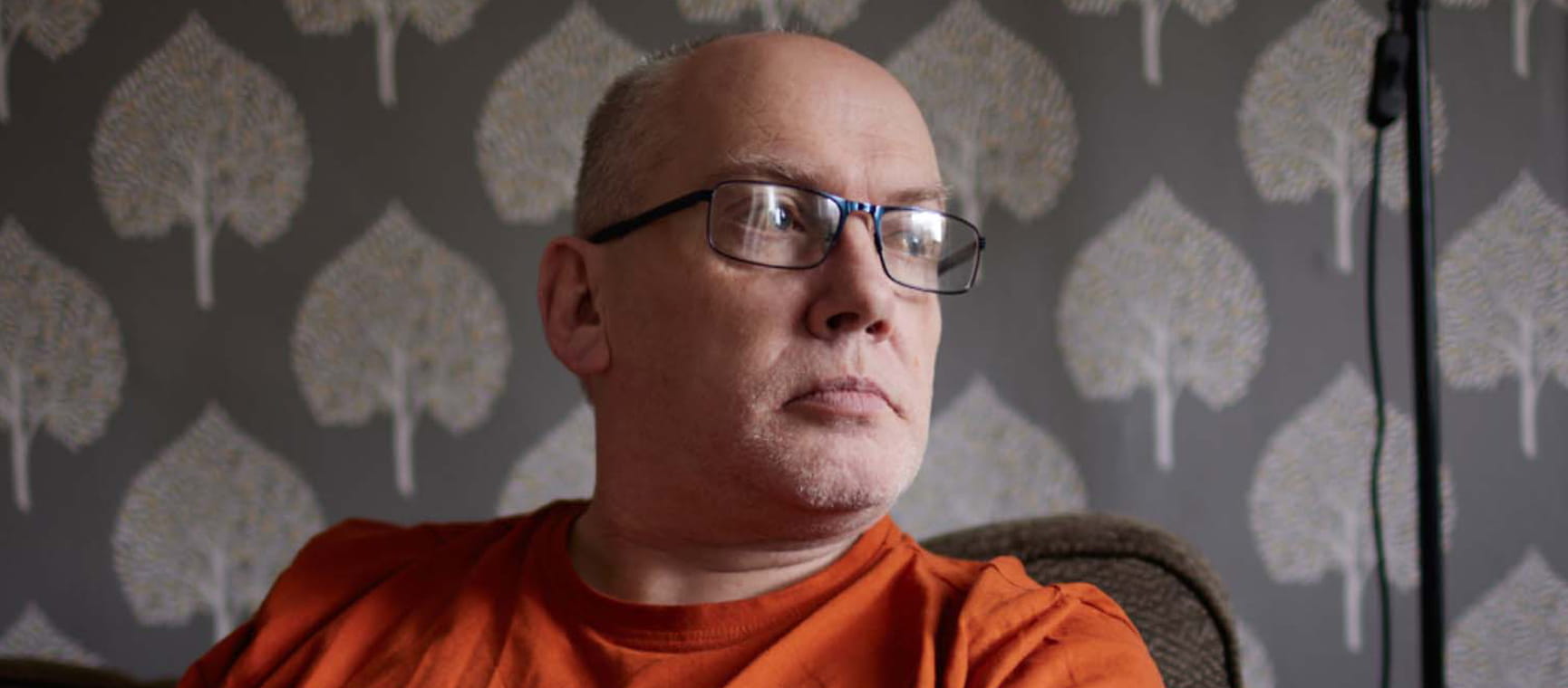 Tom Middlemass wearing glasses and an orange T-Shirt looking out a window