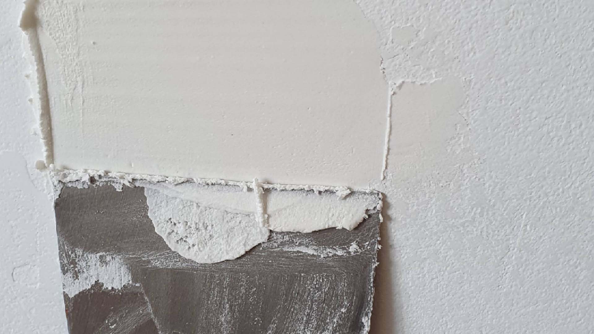 Close-up of someone applying Polyfilla to a wall using a scraper