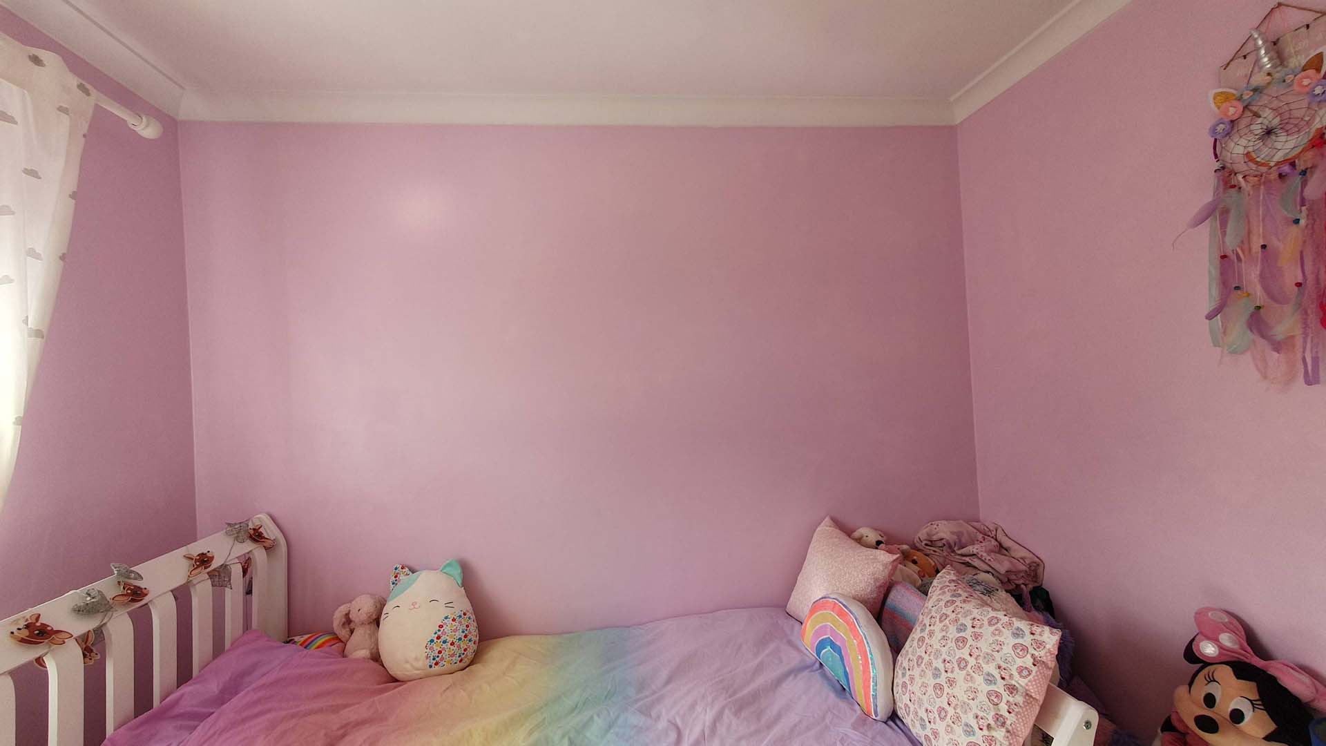 A children's bedroom with freshly painted pink walls and a double bed covered in a rainbow duvet cover