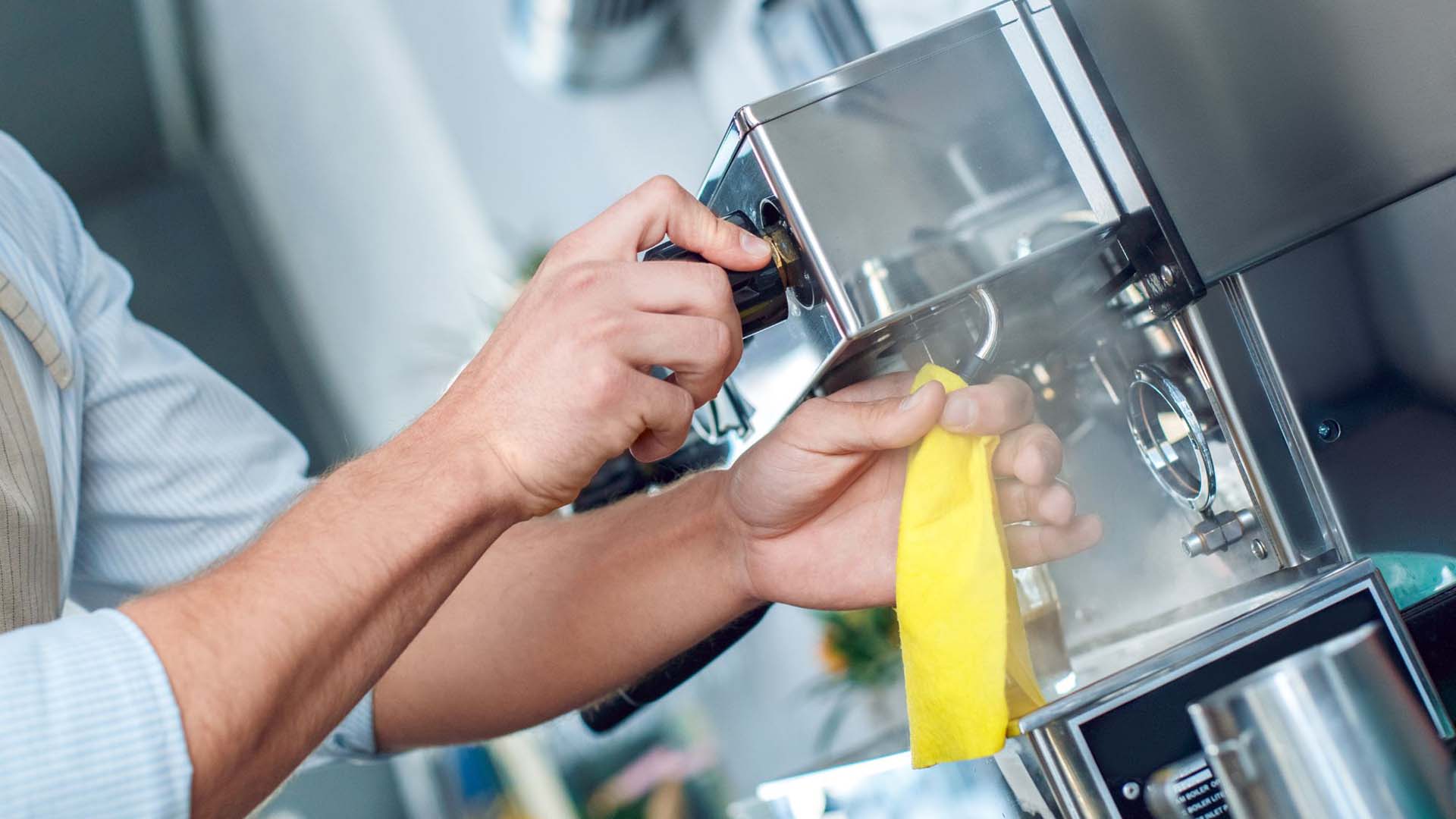 Close-up of someone using a cloth to clean the milk frother on a barista-style coffee machine
