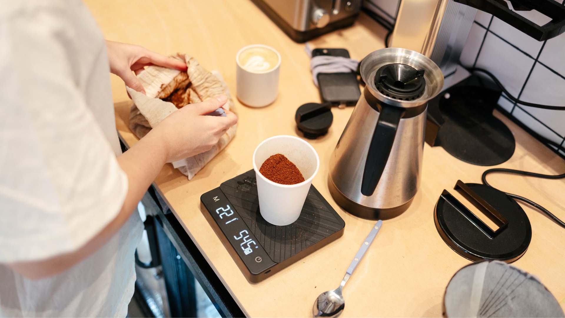 Someone weighing a cup of coffee grounds on a digital scale