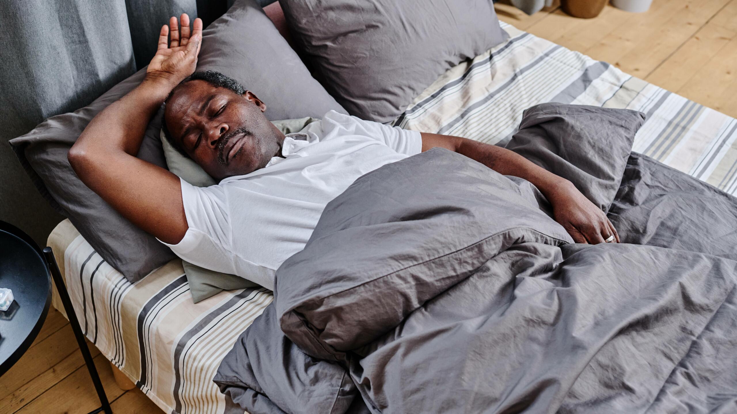 Man laying in bed asleep with his arm above his head after learning how to sleep fast