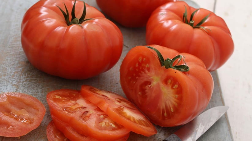 A ripe tomato cut together with others on the table next to the knife 