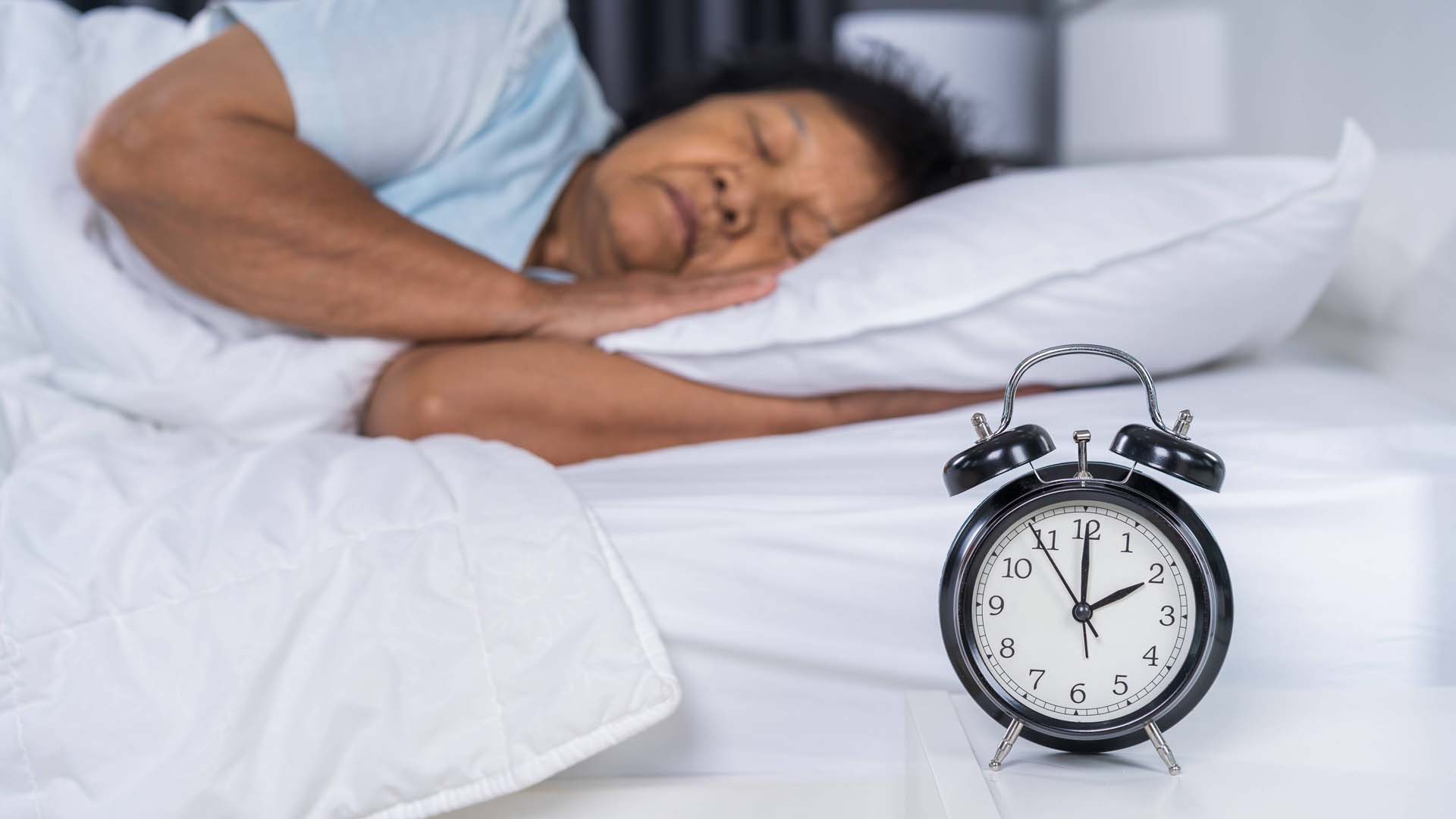 Lady asleep in bed with alarm clock in front of her