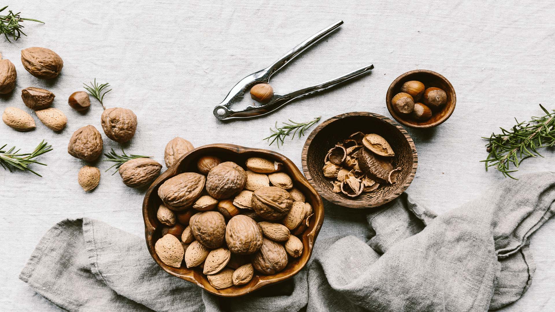 A bowl of walnuts with nuts scattered around and a set of nutcrackers on a table