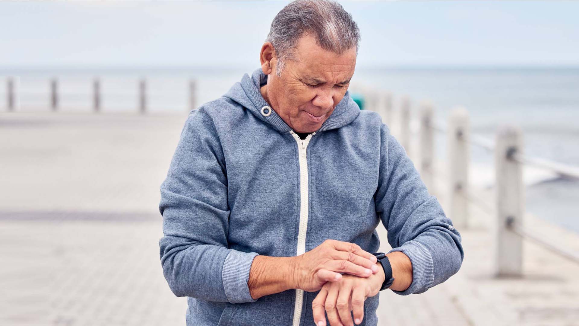 A senior man checking his fitness tracker during a workout by the seaside