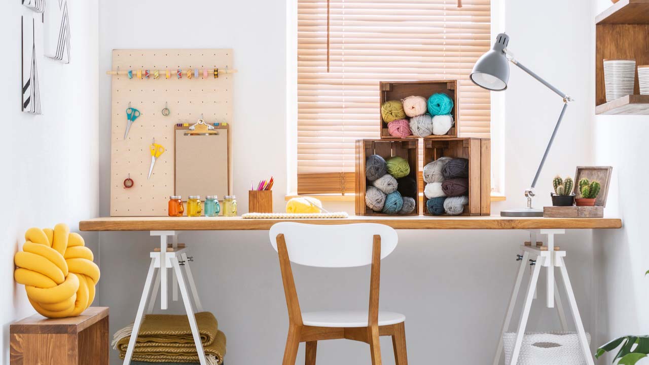 Wooden crates with dark and colorful yarn and other sewing tools on a wide workspace desk in a bright crafts room interior. Real photo.