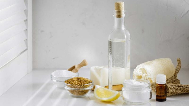 Eco friendly tools and ingredients for DIY house cleaning. White vinegar, baking soda, mustard seeds, lemon, solid natural soap, aroma oil and luffa sponge on the kitchen white table
