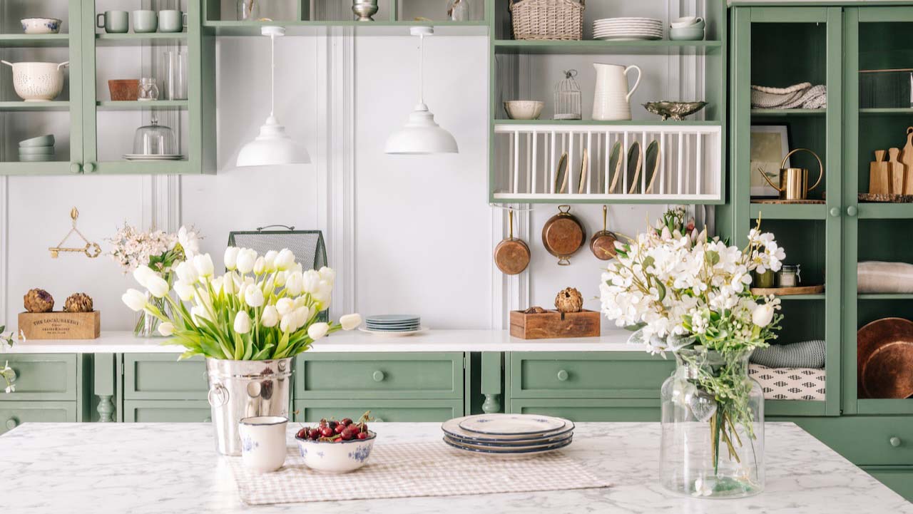 Spacious kitchen with vintage design, counter with marble top and flowers in metal bucket on it, organized furniture with various crockery, comfortable apartment interior