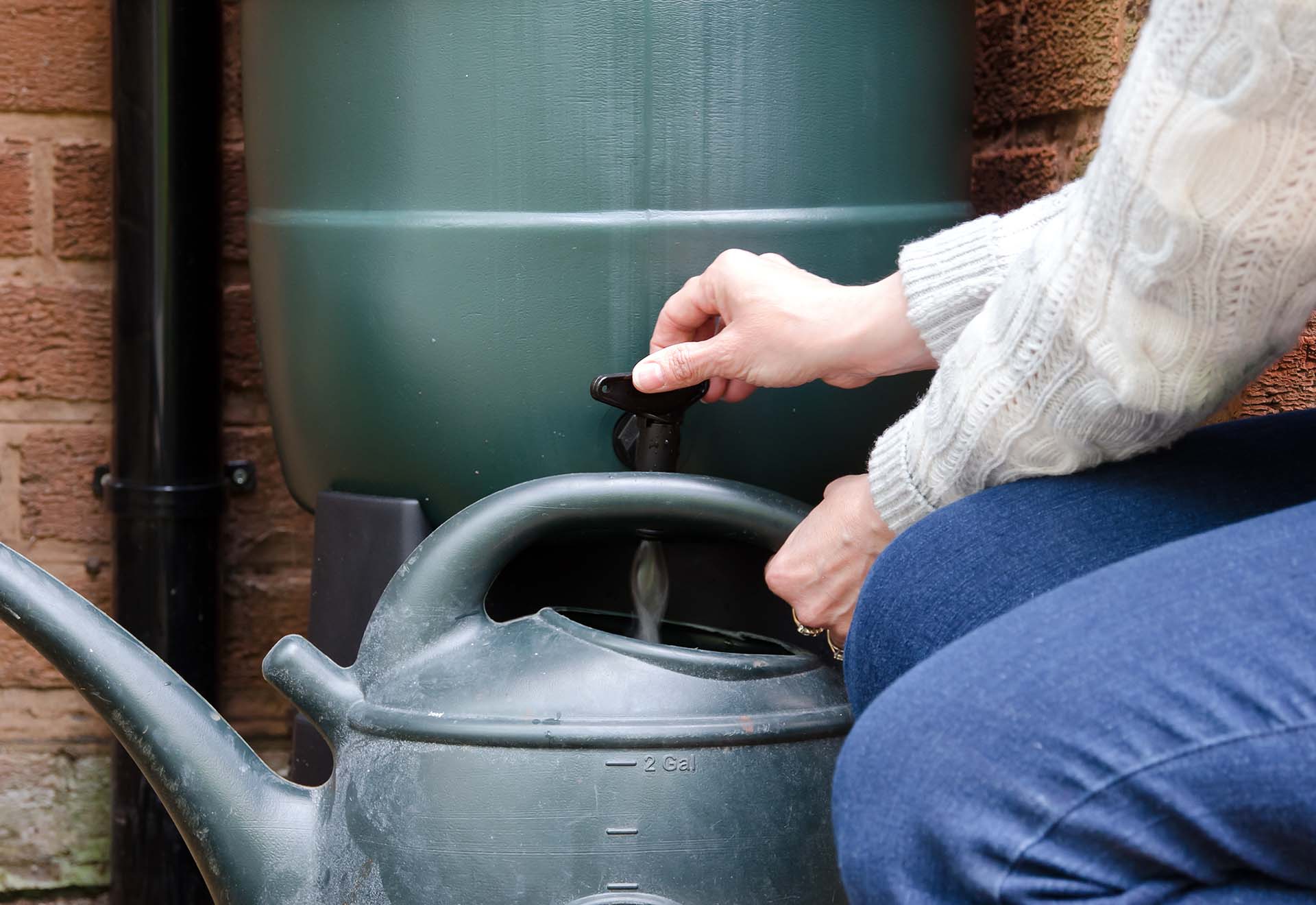 A person filling a watering can up from a water butt in a garden