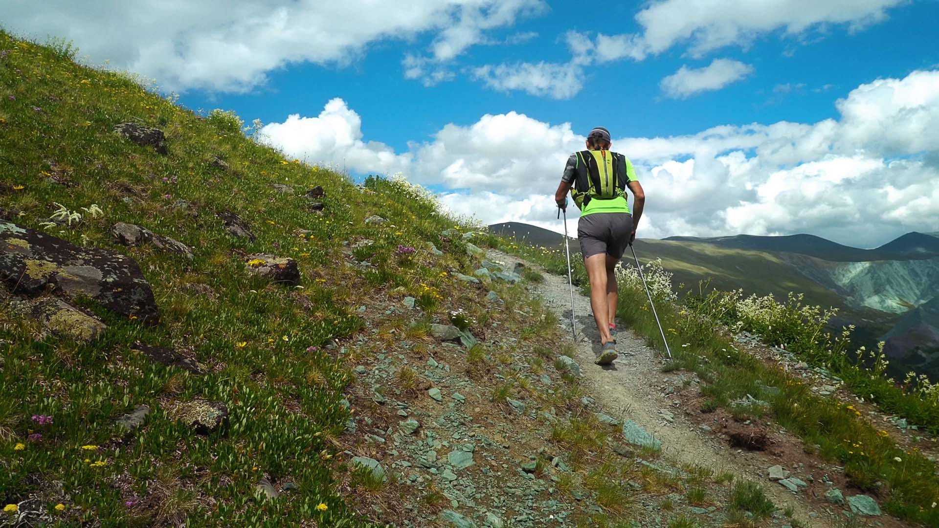 Trail ultra-runner in mountains walking with poles.
