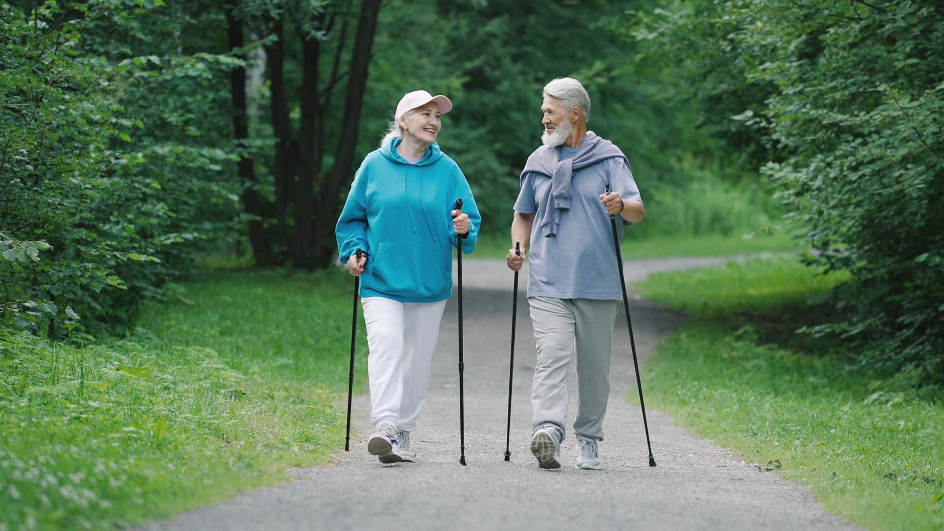 Man and a woman joyfully brisk walking together through a wood with walking poles