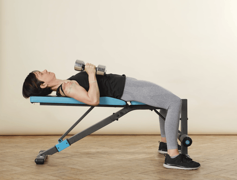Woman lying on bench pressing a pair of dumbbells overhead
