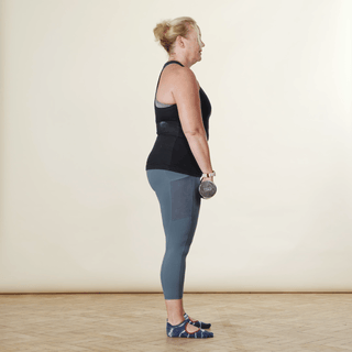 A woman in sports clothing demonstrating a deadlift with dumbbells