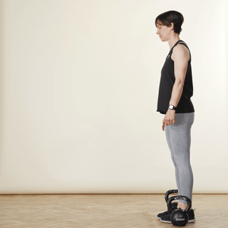 A woman in sports clothing demonstrating a carry exercise with kettlebells