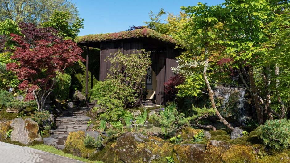 Hanare - a small house separated from the main building, in the middle of several colorful trees, plants, and stones, with a small stone path leading to the door