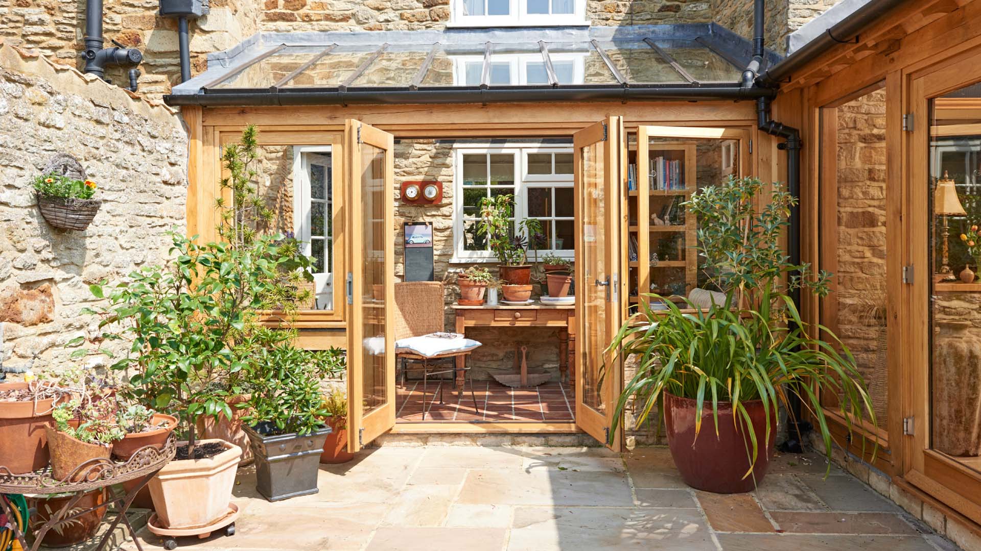 A wooden garden shed with glass doors and windows opening onto a patio