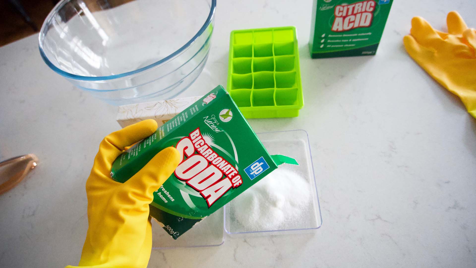 A hand in a yellow glove mixes ingridients