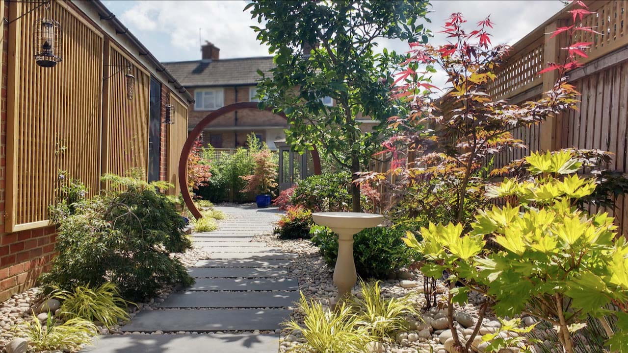 A moon gate - a corten steel circular passageway at the threshold of a garden stone pathway in the middle of Pebbles, Acers and grasses