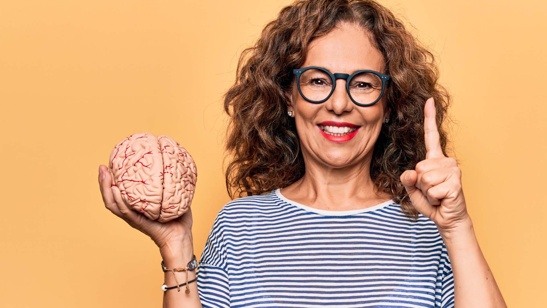 A woman holding a brain in her right hand while holding up one finger on her left hand.