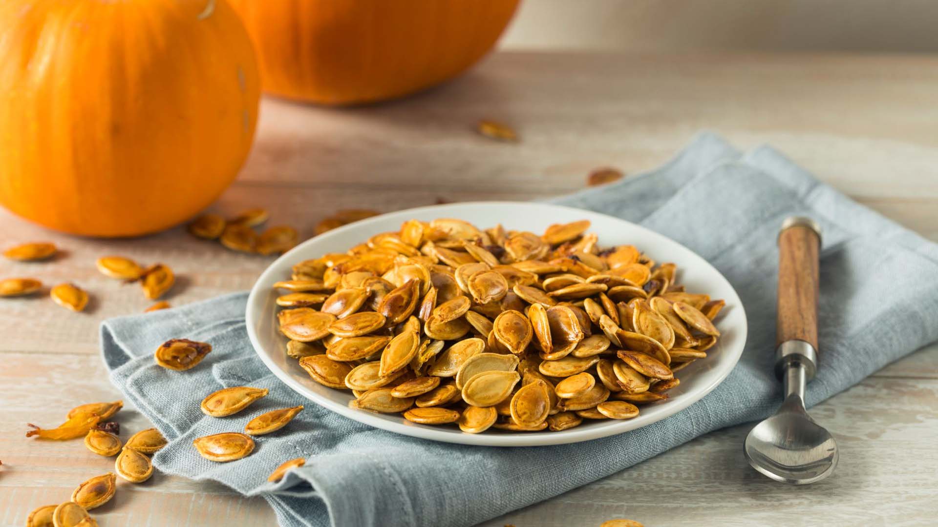 Pumpkin seeds in a dish next to some pumpkins