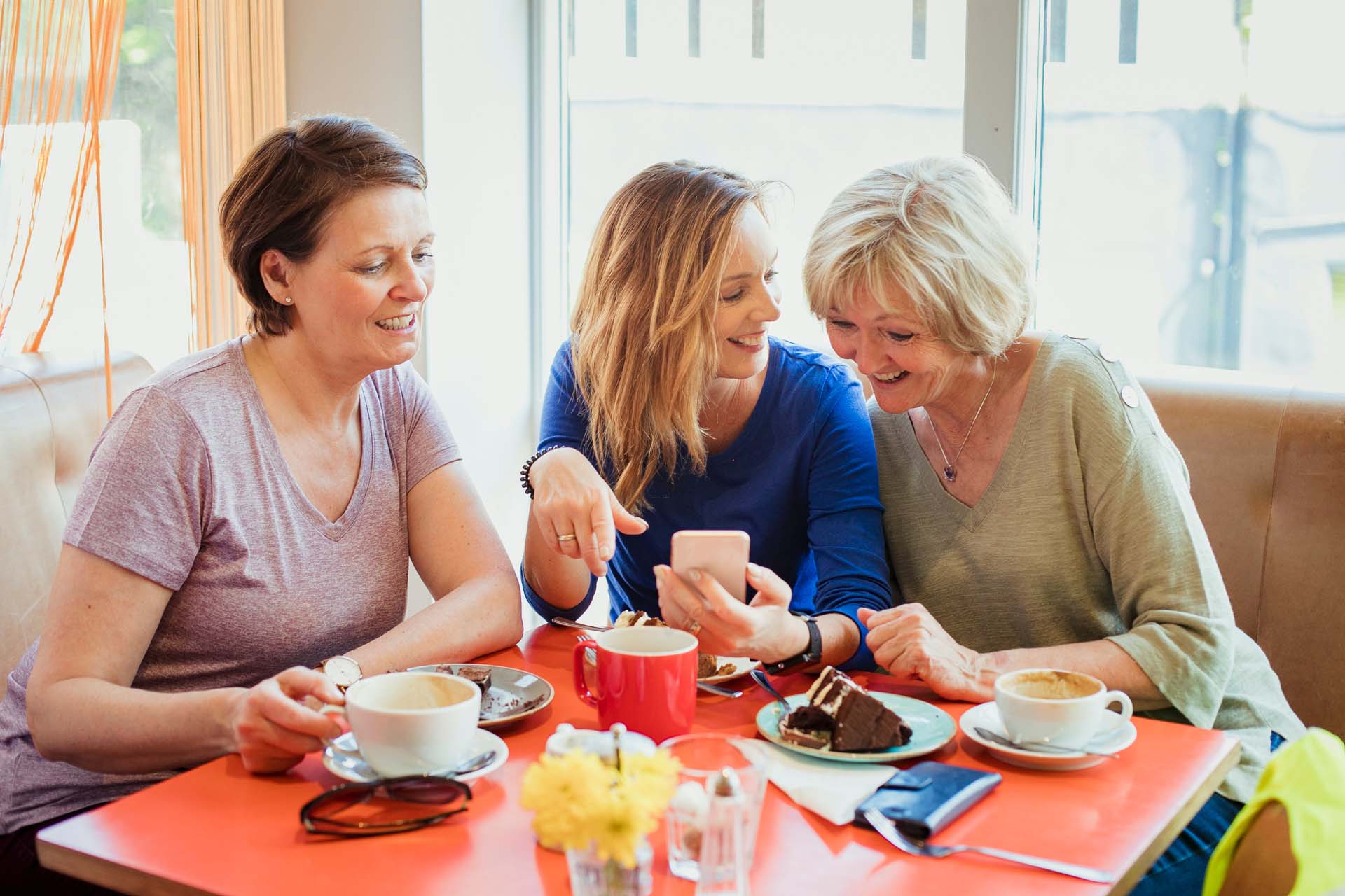 Three female friends enjoying coffee in a cafe environment while looking at a phone