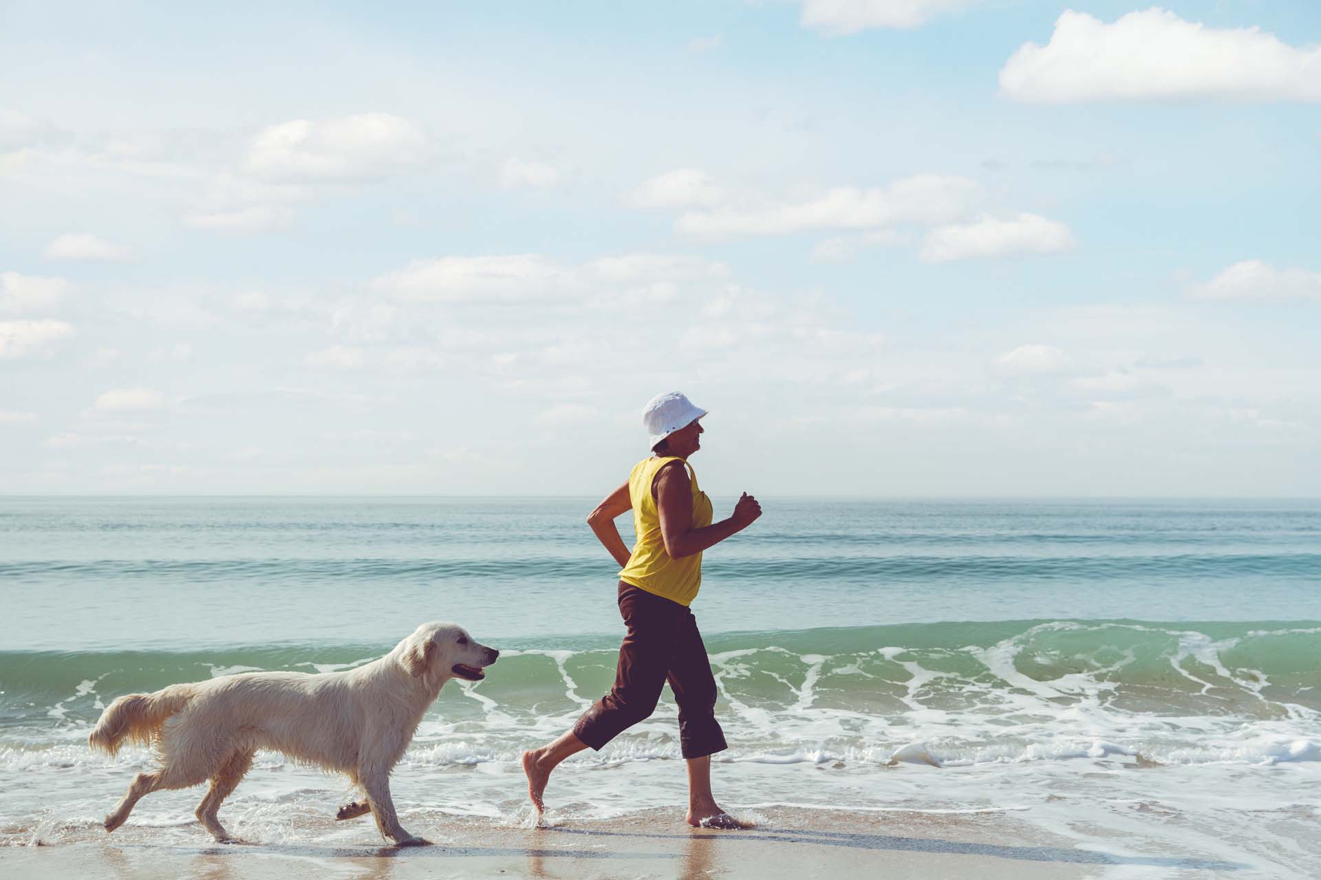 A woman running along a beach with her dog