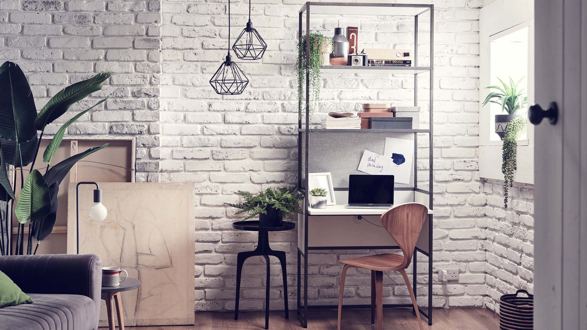 A small home office desk with shelving above against a white brick wall
