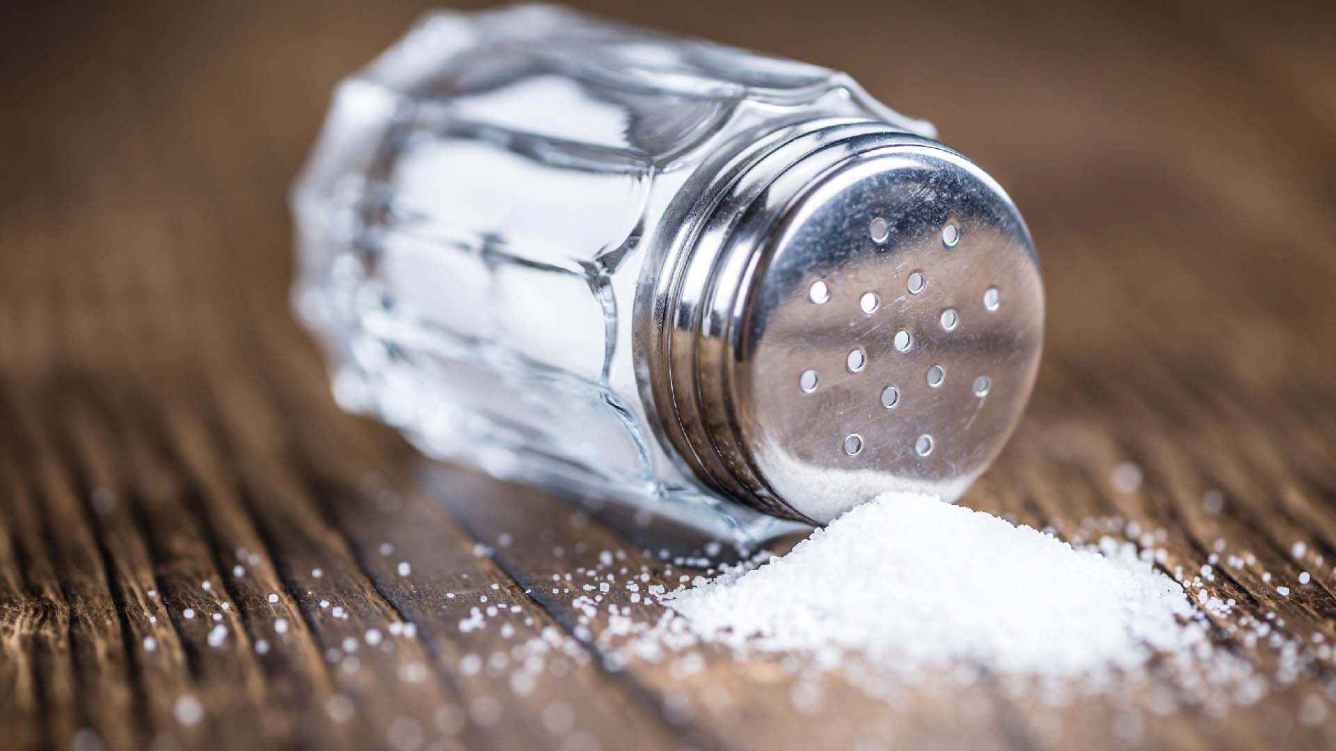 A salt shaker on its side on a dark wood table