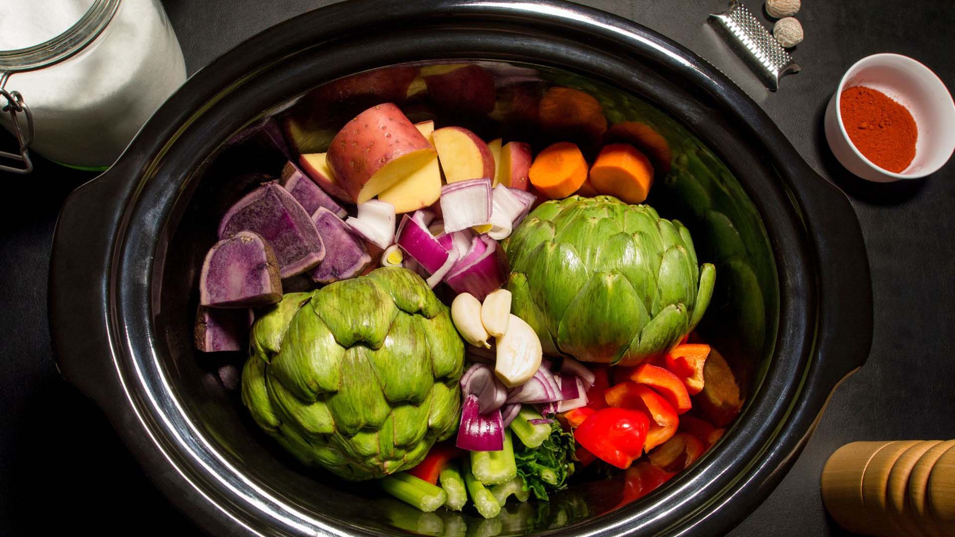 Vegetables including carrots, sweet potatoes and artichoke in a slow cooker