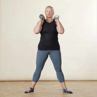 A woman in sports clothing demonstrating a squat while holding weights above her shoulders