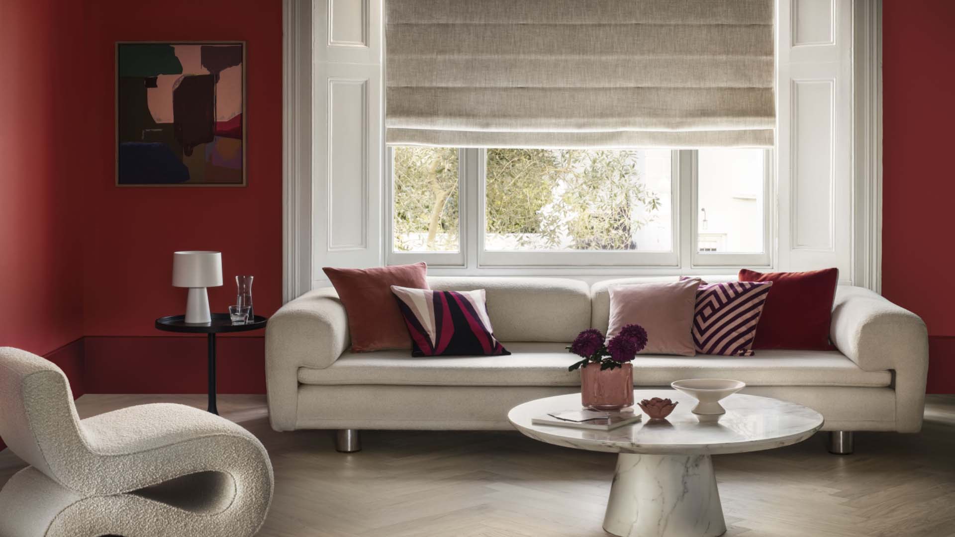 A room with dark red walls, a cream sofa and big bright windows