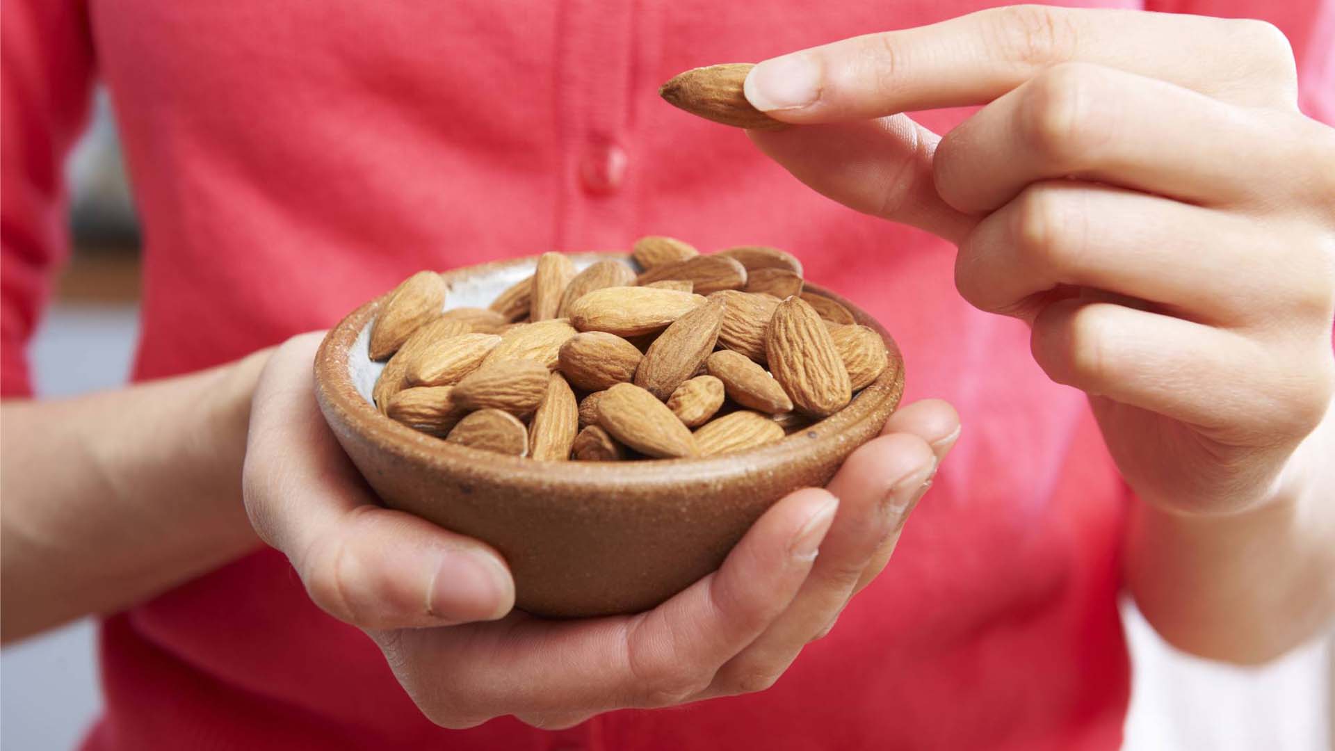 A woman picking up an almond from a bowl of almonds