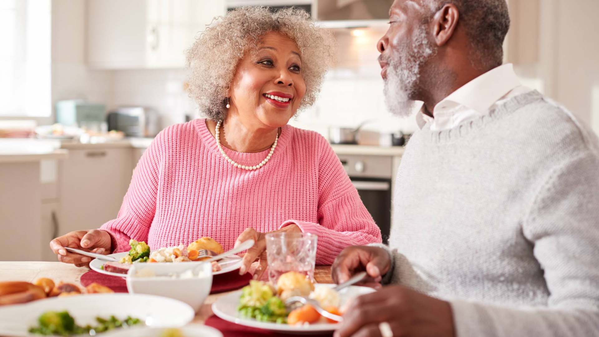 A happy older couple share a healthy meal at a kitchen table