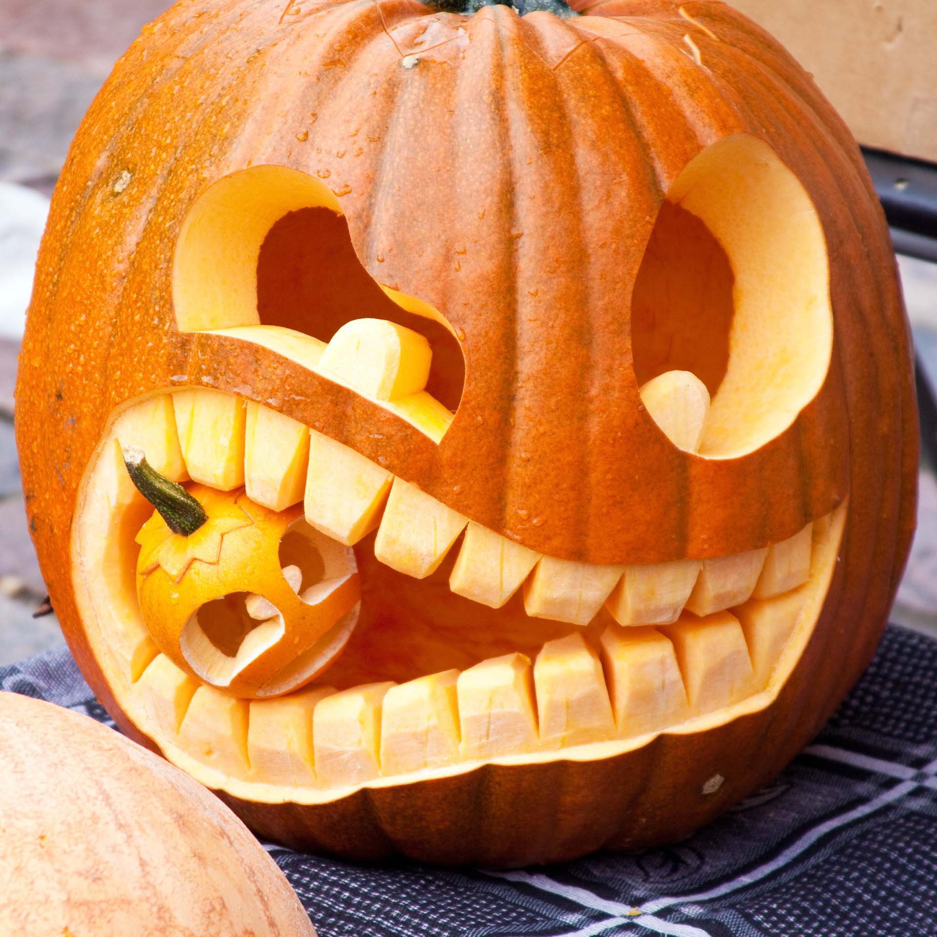 A carved pumpkin that looks like it is eating a smaller pumpkin
