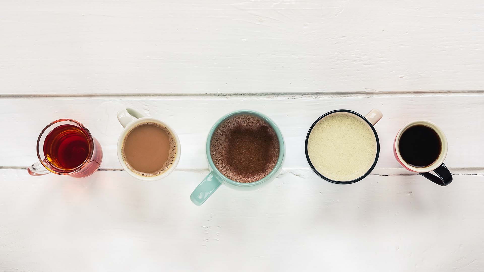 Five hot beverages shot from above, in different colourful mugs and cups