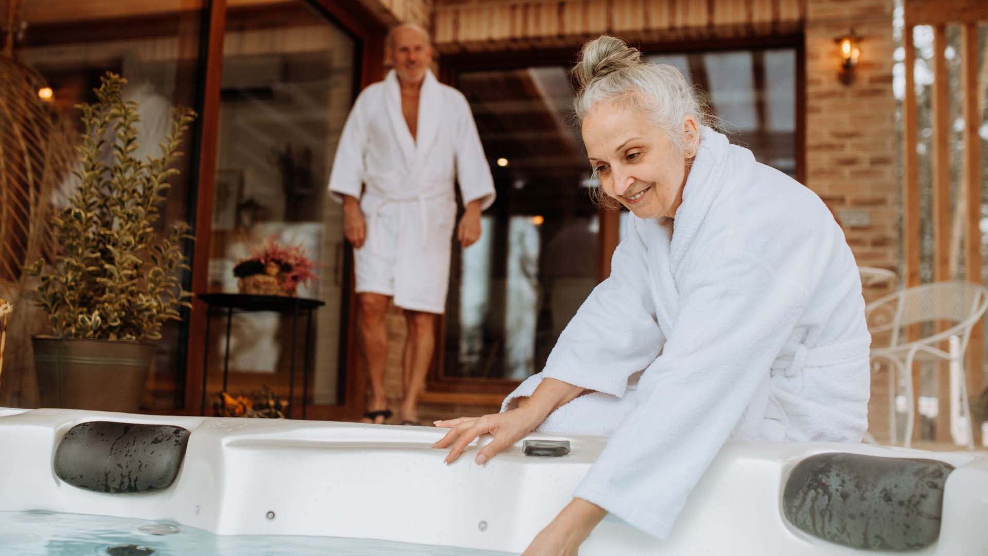 Woman and a man in white robes getting into a hot tub