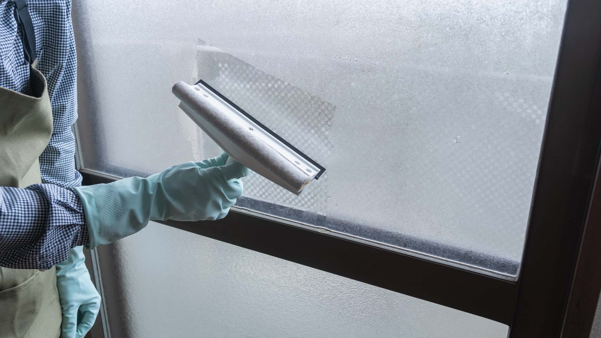 A oerson cleaning condensation off a window with a squeegee