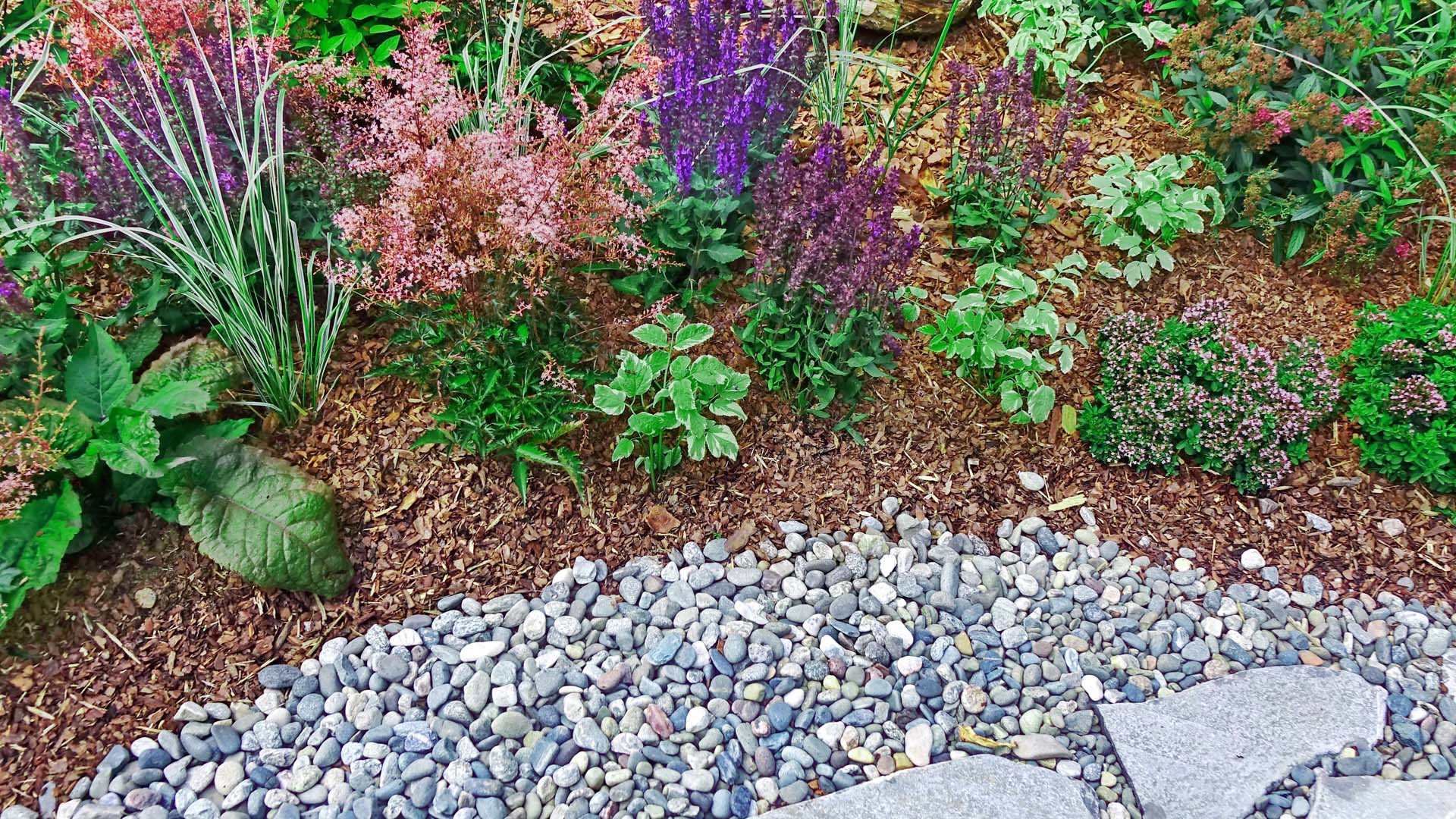 The stone and gravel pathway gently merges with vibrant, blossoming flower beds
