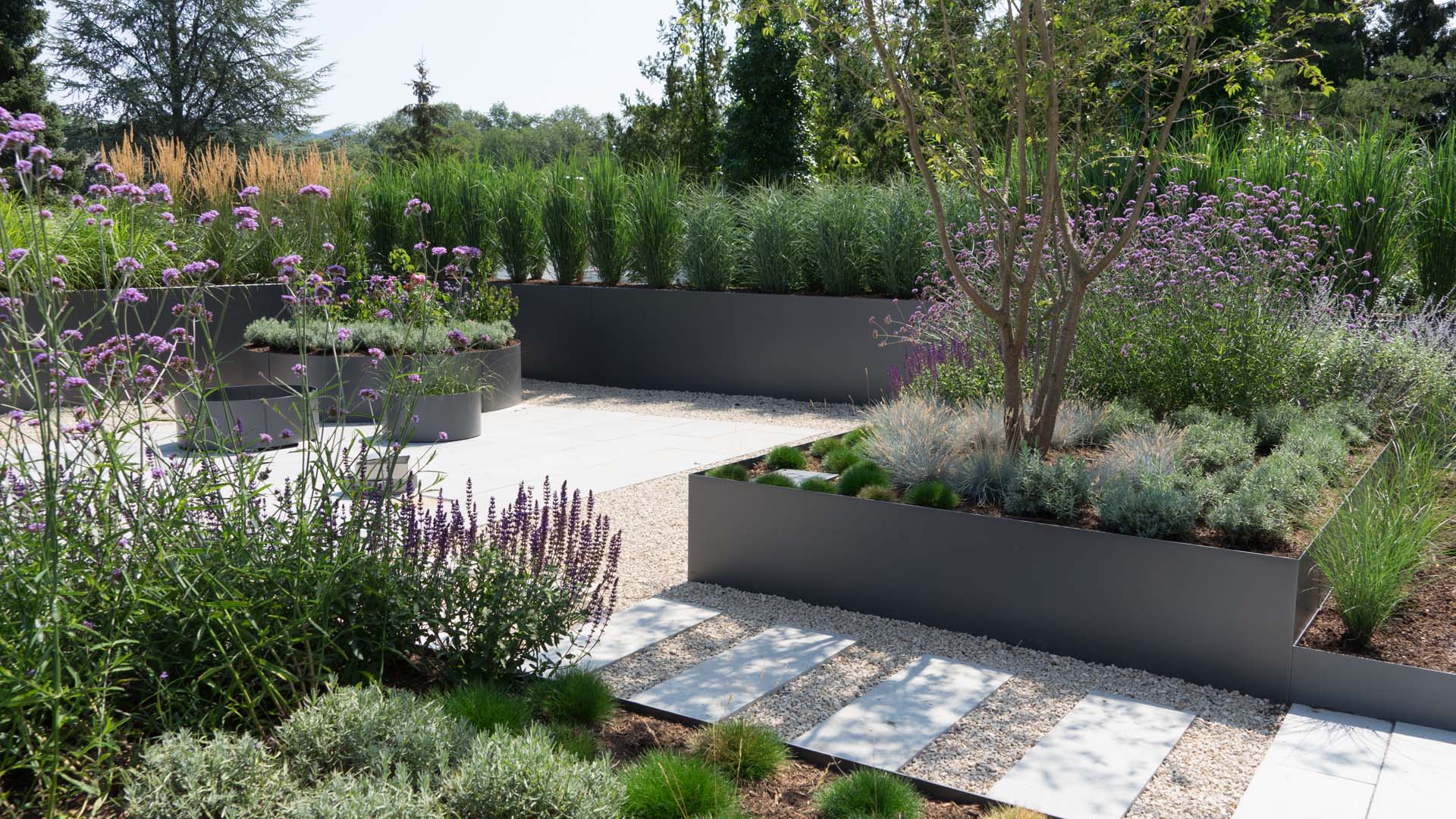 Spacious gravel garden features numerous raised beds filled with a variety of plants and trees, making it easier to maintain and keep tidy