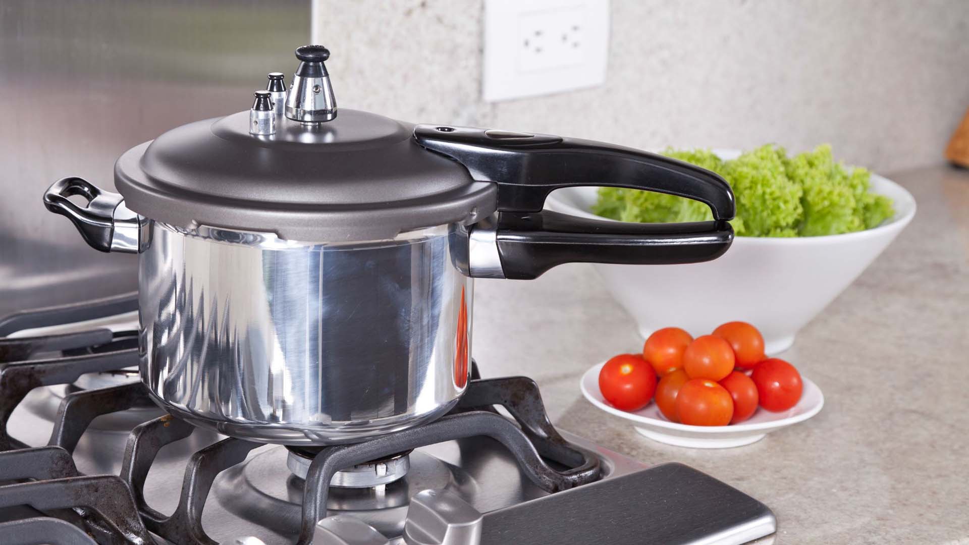A stove-top pressure cooker on the hob with food items in the background