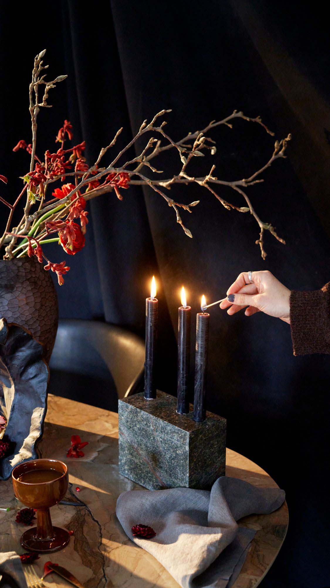 Someone lighting three navy candles in a marble candle holder as part of a festive table setting