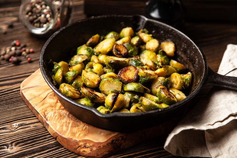 A pan of cooked Brussels sprouts on a wooden shopping board