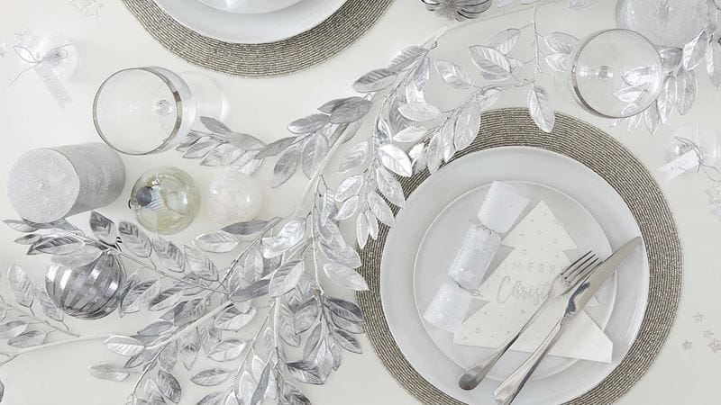 A festive table setting with silver accents including silver foliage, baubles and white Christmas crackers