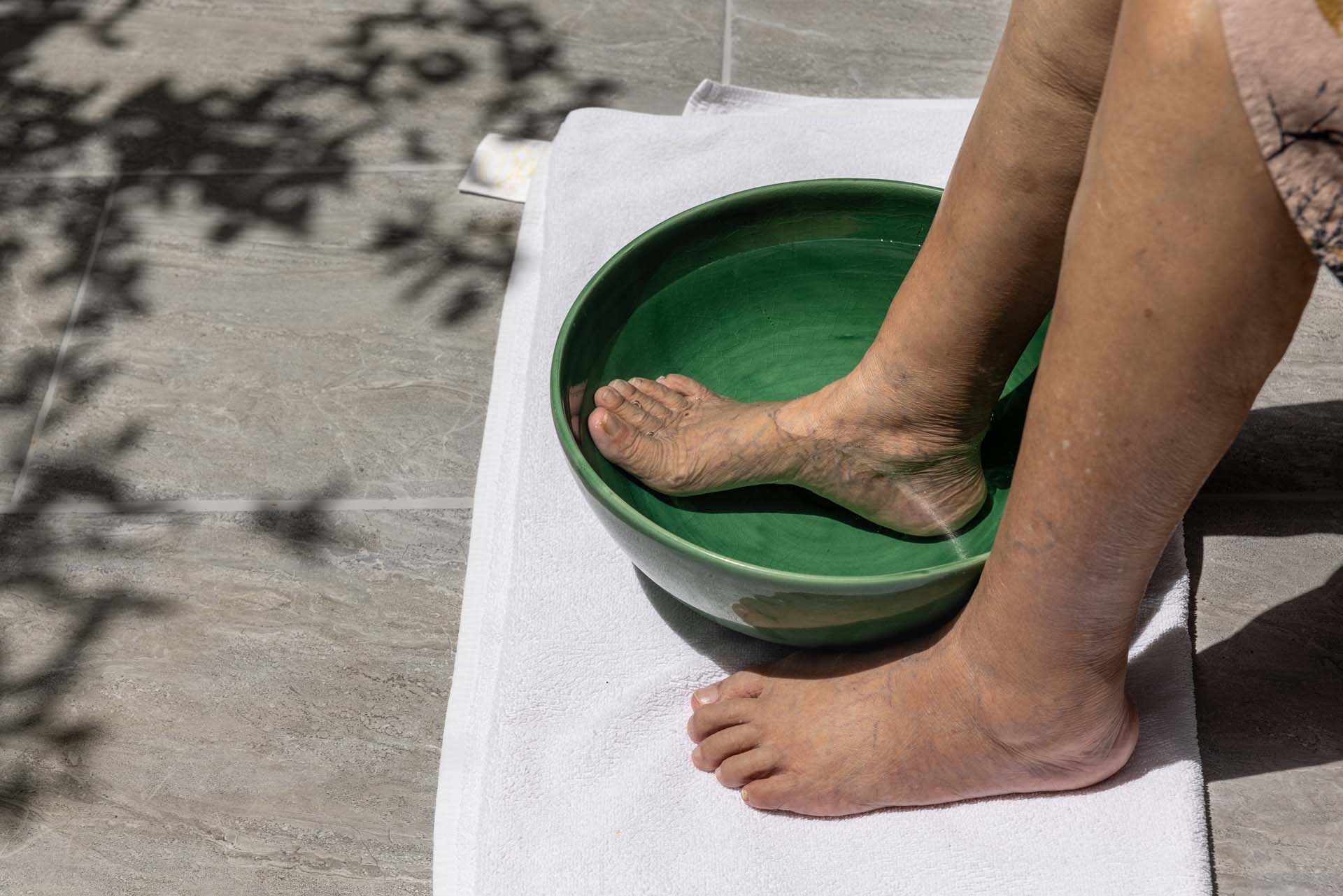 A woman soaking her feet in water in a small green bowl with a towel underneath it
